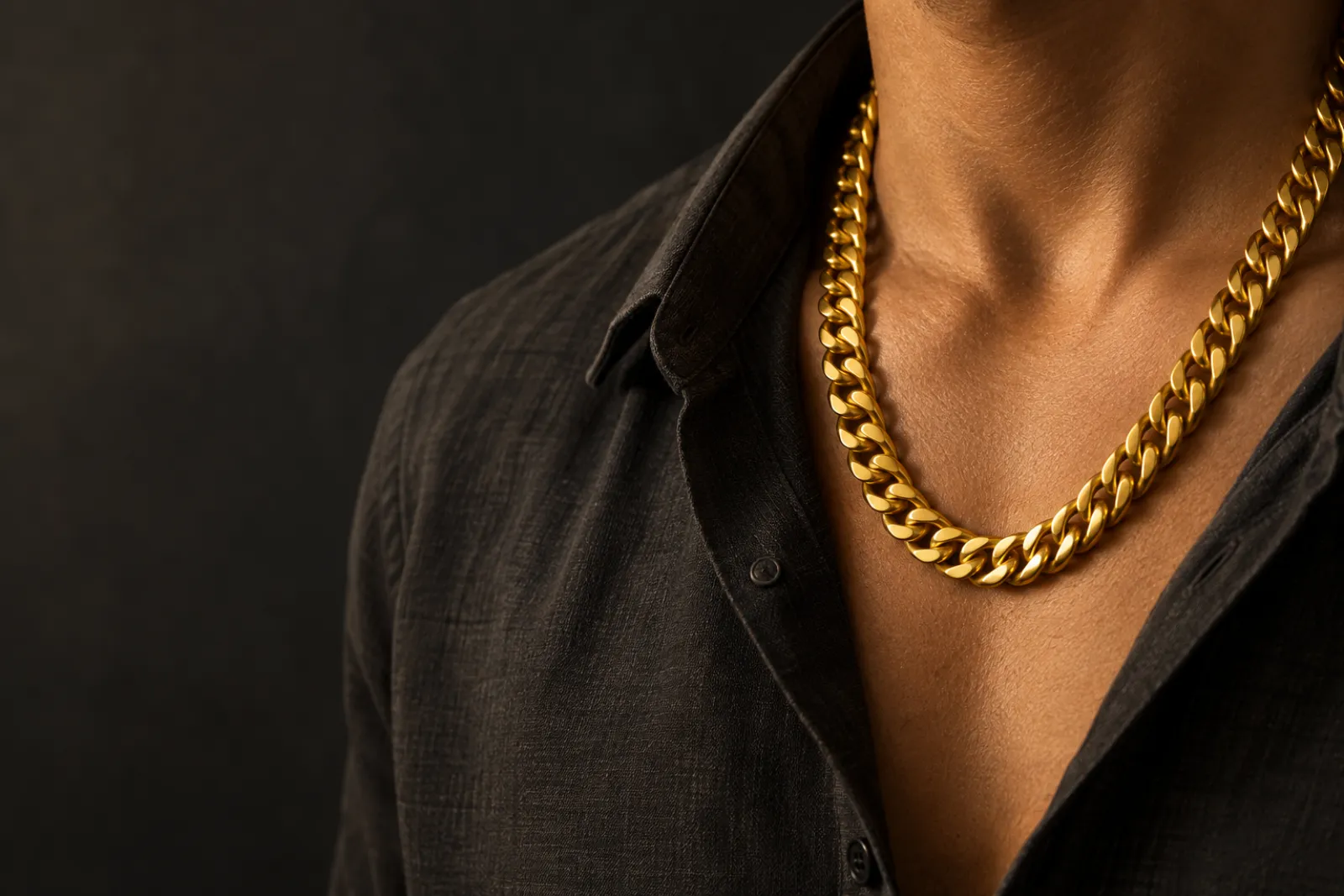 Heavy 24K gold chain worn at the collarbone over a dark shirt in warm light